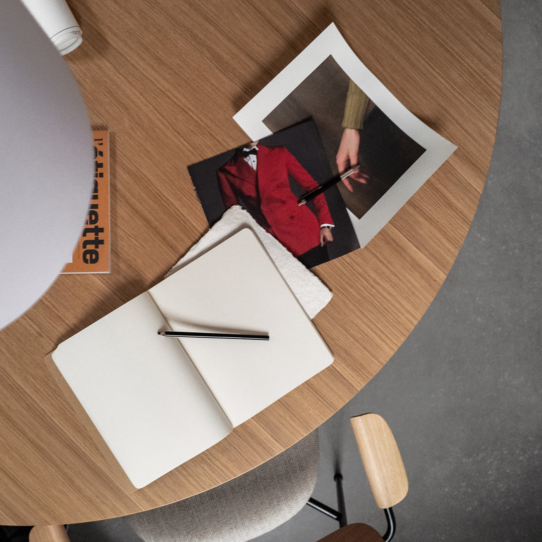 Open white notebook on a wooden table with colorful fashion images and a sleek black pen. Modern and stylish arrangement.