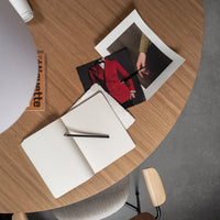 Open white notebook on a wooden table with colorful fashion images and a sleek black pen. Modern and stylish arrangement.