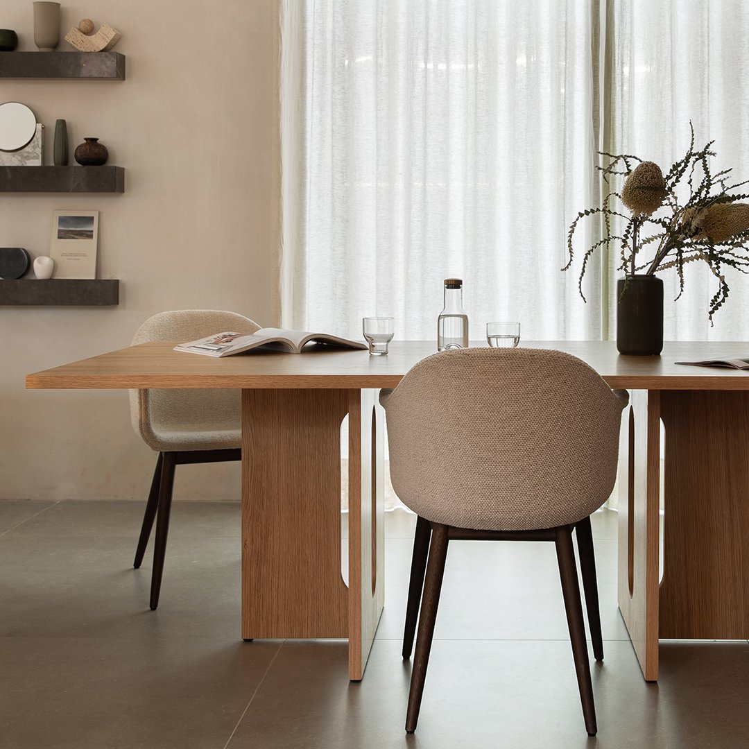 Neutral-toned chair with soft fabric upholstery, paired with a light wood table, set against a calming, textured backdrop.