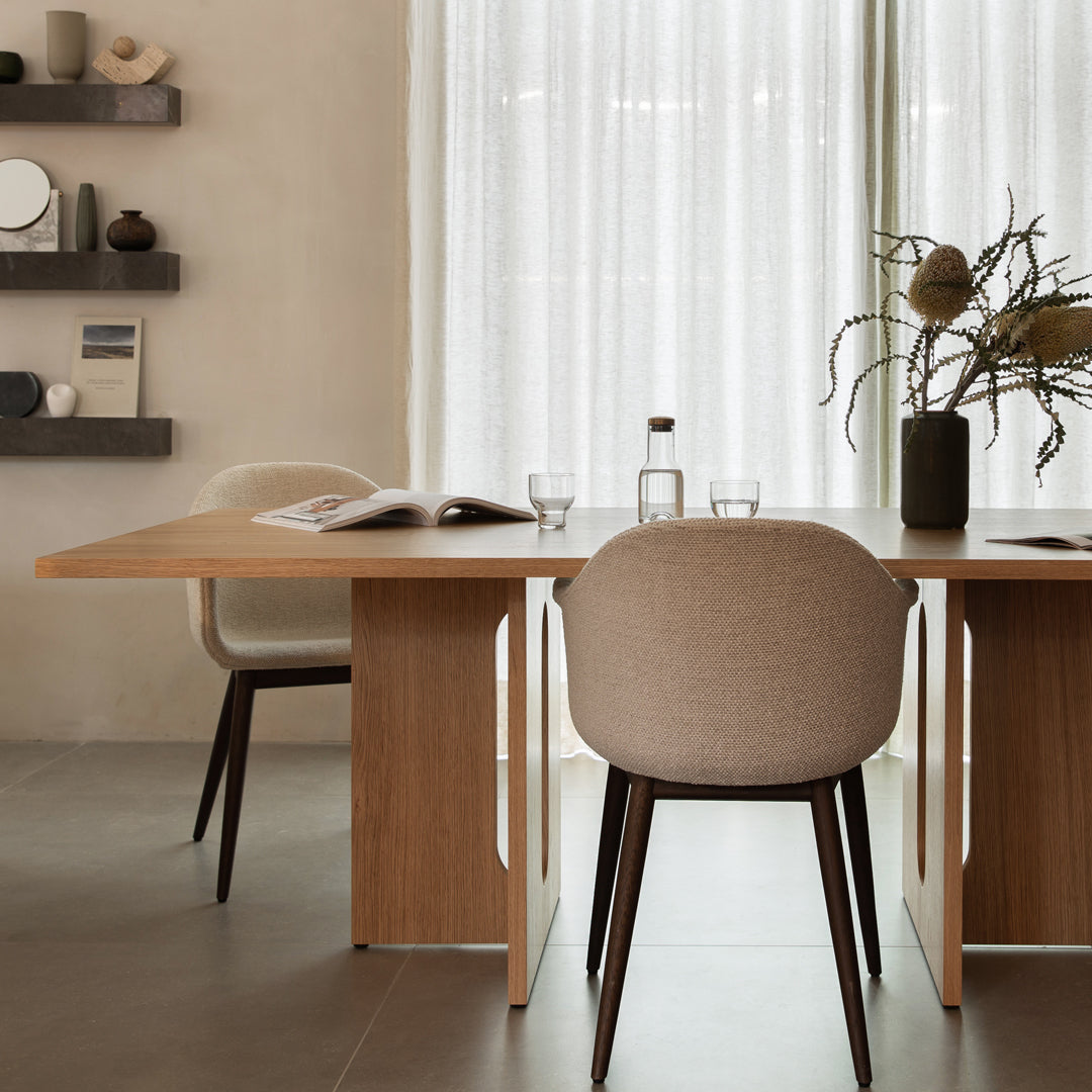 Minimalist dining setting with warm wooden tones, beige chair upholstery, and soft, neutral curtains.