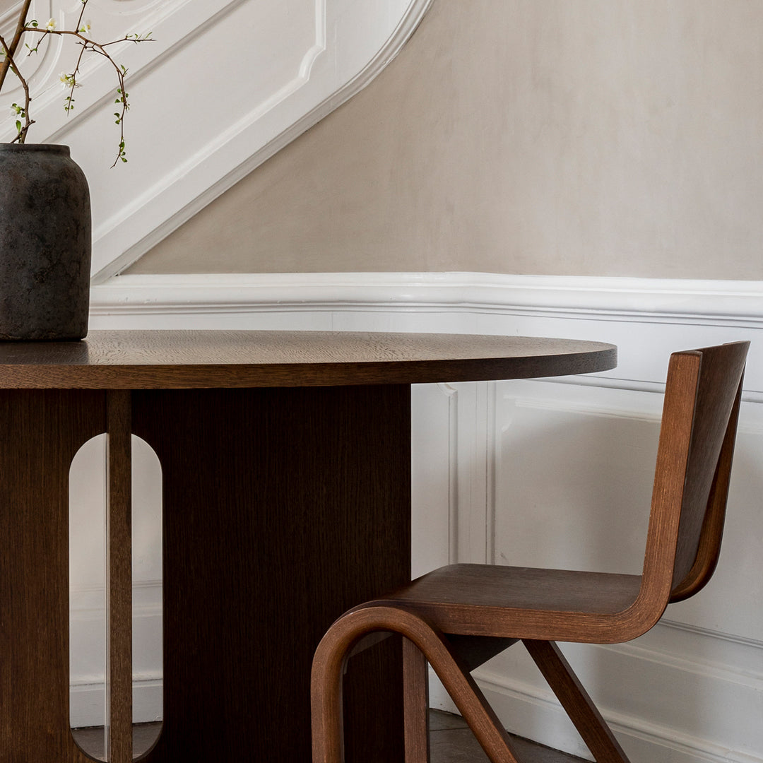 Wooden dining table and chair in rich brown tones with smooth, curved shapes and minimalist design.