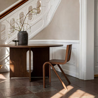 Wooden round table in rich brown with minimalist chair, complemented by a dark gray vase and soft, neutral wall tones.