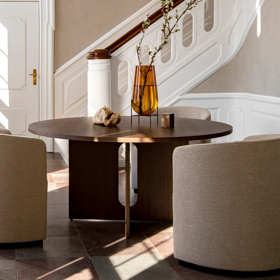 Round dark wood table with soft beige accent chairs, featuring a minimalist design and warm natural tones.