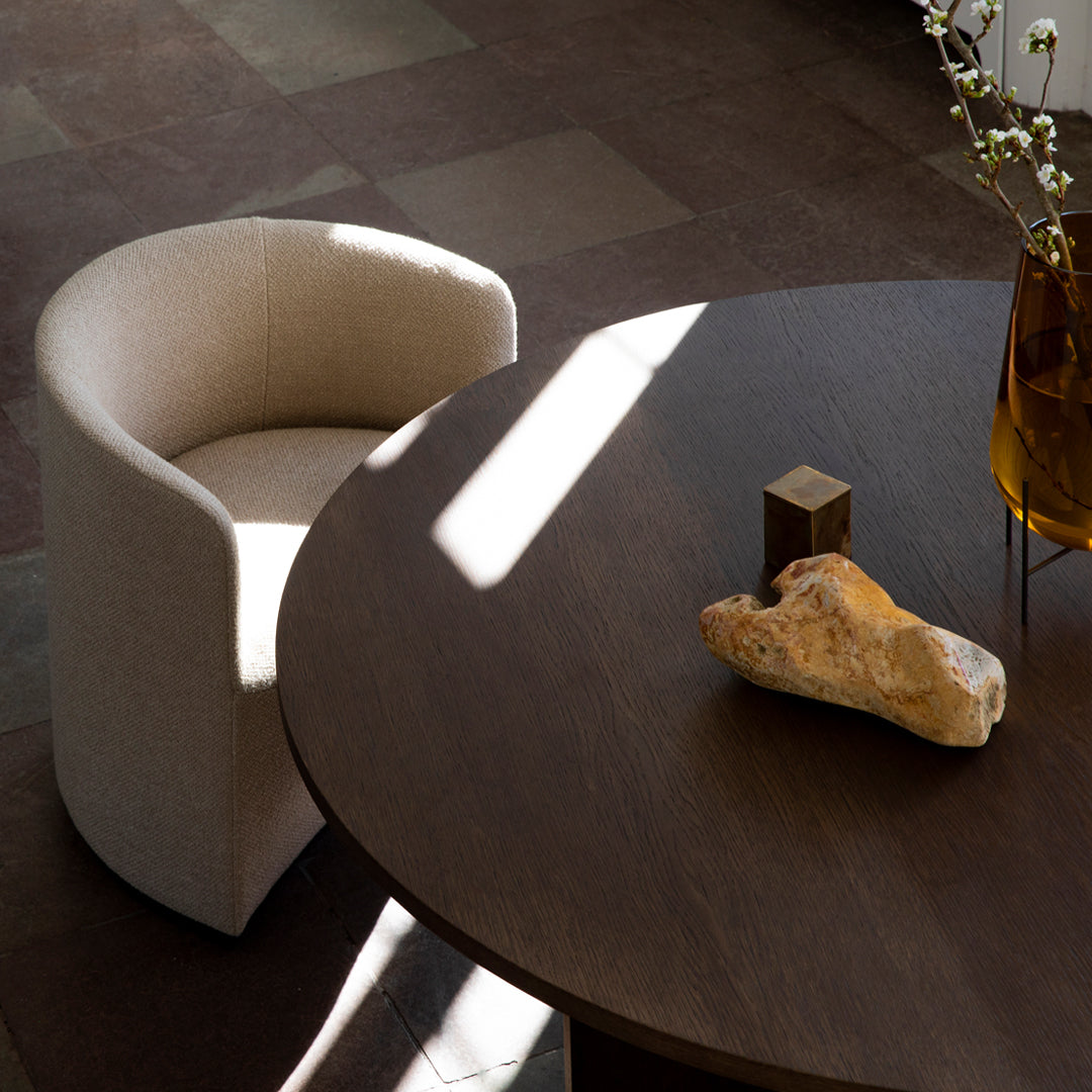 Beige upholstered chair beside a round dark wooden table, with natural stone accents and soft lighting.
