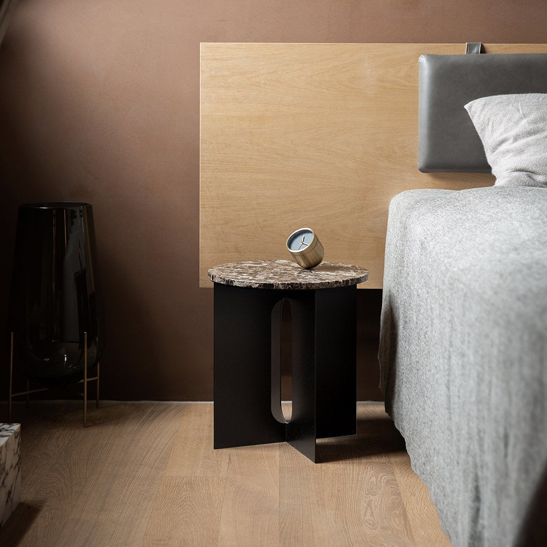 Black side table with a textured stone top, contrasting with a warm brown wall and light gray bedding.
