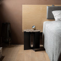 Black side table with a textured stone top, contrasting with a warm brown wall and light gray bedding.
