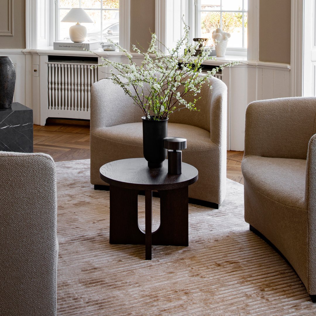 Beige armchairs with a subtle textured pattern, dark wooden table, and light neutral rug with soft stripes.