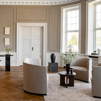 "Neutral-toned room with beige chairs, light wood flooring, and soft greenery accents, creating a calm, minimalistic vibe."
