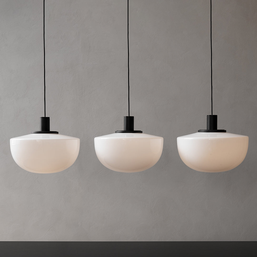 Three rounded frosted white glass pendant lights with sleek black metal fixtures, creating a modern and minimalist aesthetic.