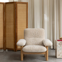 Cream-colored upholstered armchair with soft textured fabric and natural wood legs, set against a neutral backdrop.