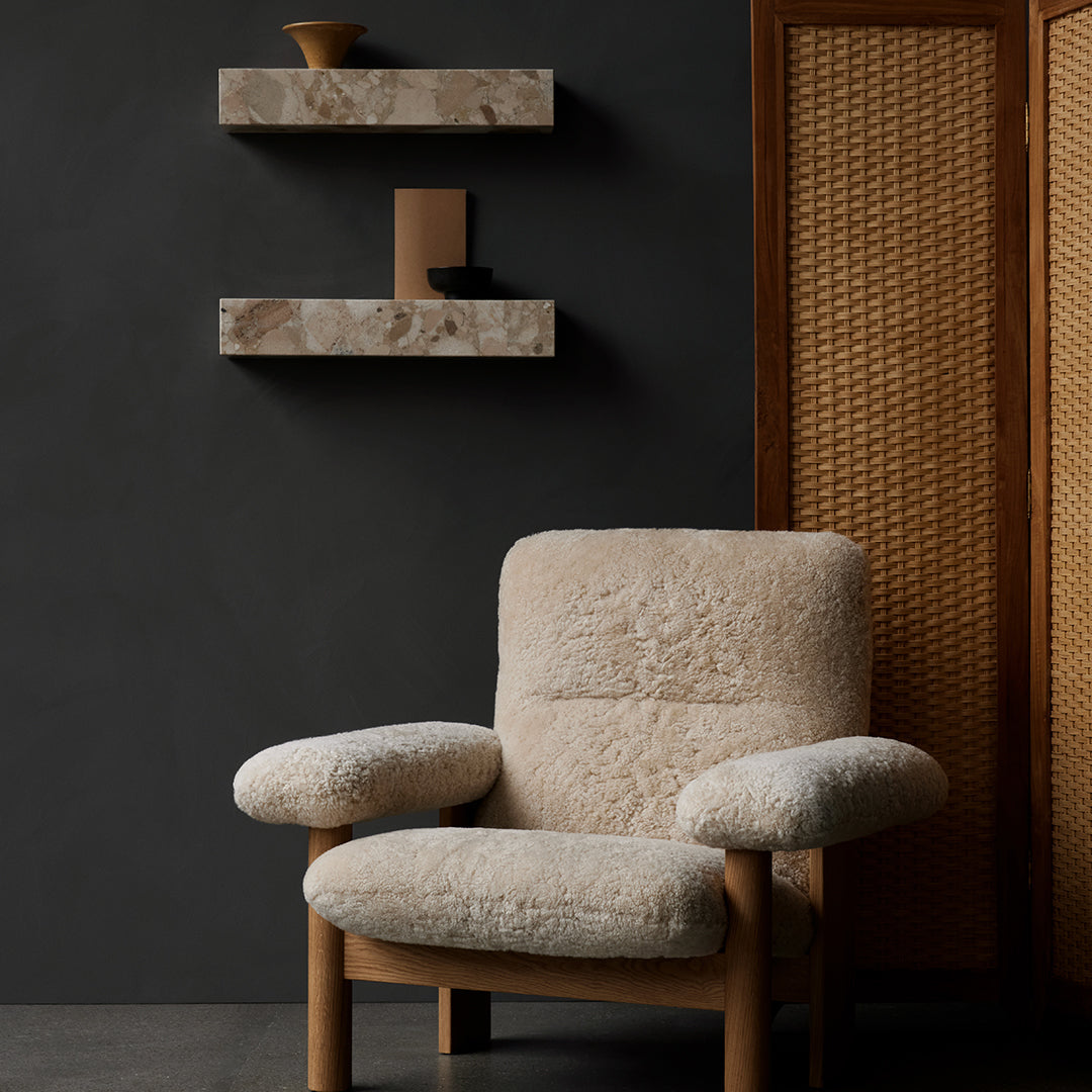 Beige textured chair against a dark wall, featuring stone shelves and woven elements for a cozy modern aesthetic.
