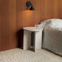 Minimalist white side table with a smooth round top and sleek cut-out design, set against a warm wood-paneled wall.