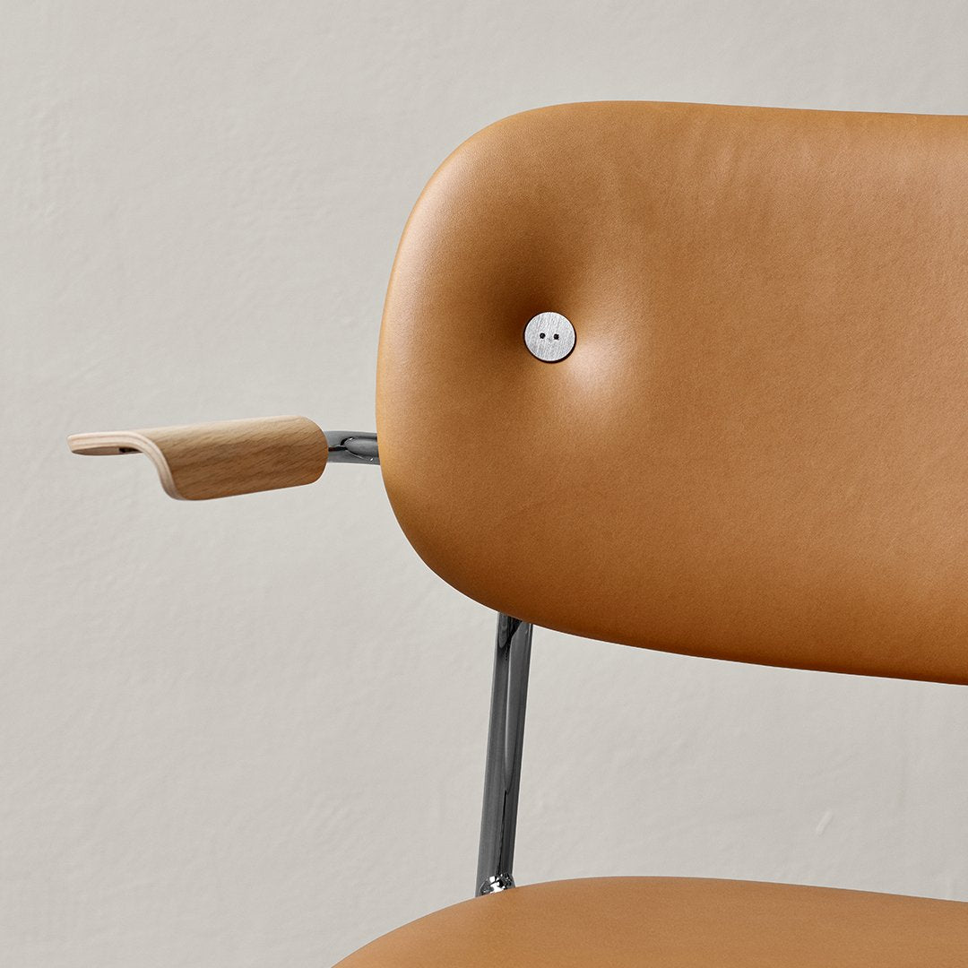 Tan leather chair with a button tuft and sleek metal armrest, featuring minimalist design and modern aesthetics.