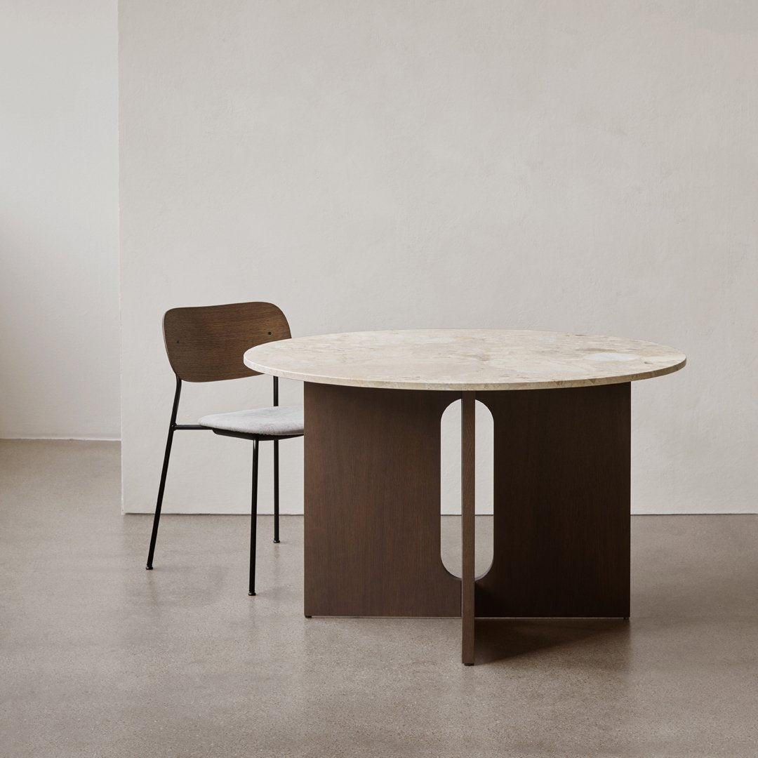 Round marble table with a dark wood base and a minimalist design, paired with a light wood chair against a neutral backdrop.