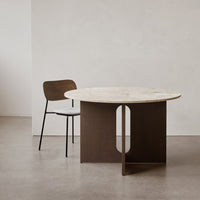 Round marble table with a dark wood base and a minimalist design, paired with a light wood chair against a neutral backdrop.