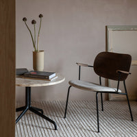 Modern chair with a brown seat and black frame, paired with a round marble table and textured neutral rug.