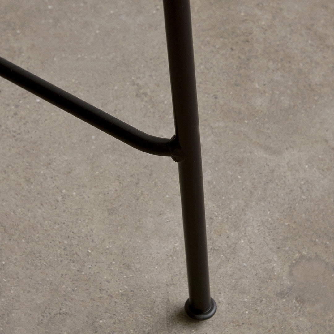 Black metal chair leg with a sleek, industrial design against a textured concrete surface.