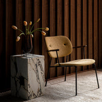 Stylish tan chair with black metal frame, paired with a textured marble pedestal and a neutral-toned background.