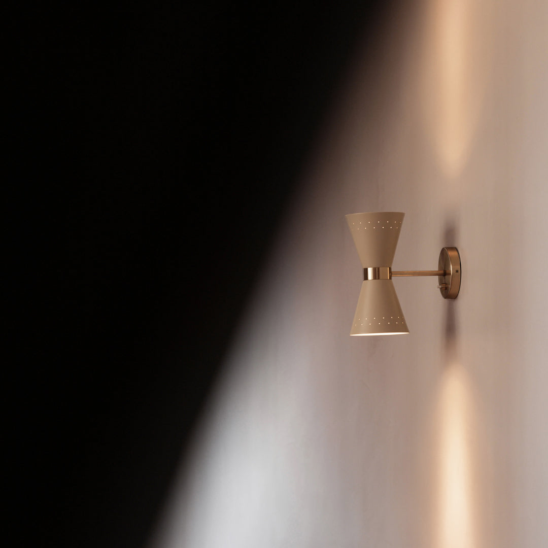 Golden wall sconce with a textured, hourglass design casting soft light against a warm-toned wall.
