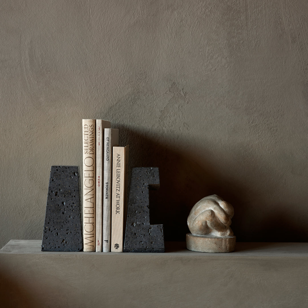 Black textured bookends with neutral-colored books and a light stone sculpture against a muted background.