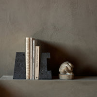 Black textured bookends with neutral-colored books and a light stone sculpture against a muted background.