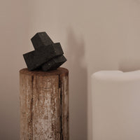 "Black geometric decor on a rustic wood stump against a soft neutral background."