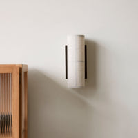 "Minimalist cylindrical wall sconce in soft beige with black accents on a light wall background."