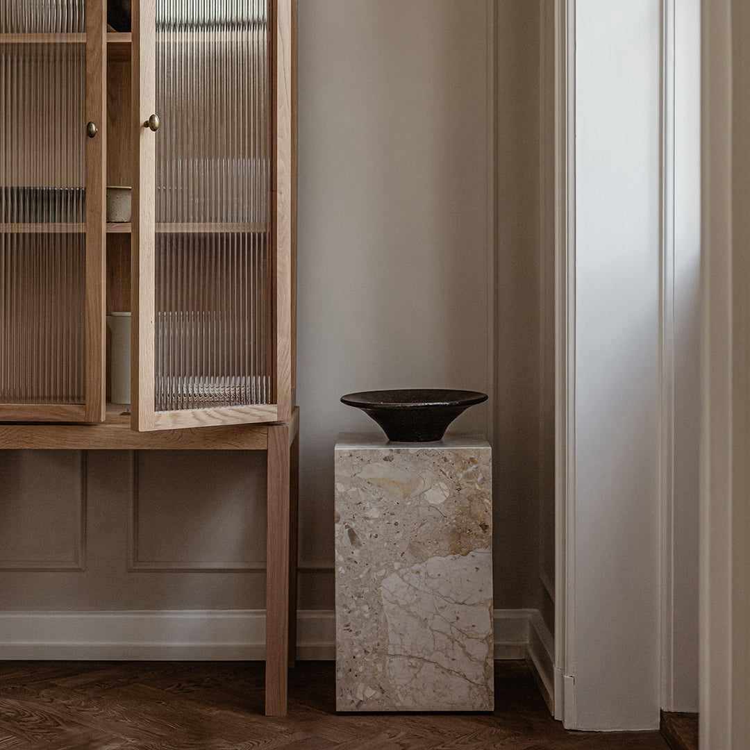 Natural stone pedestal with a textured surface, featuring soft beige tones and subtle gray veining against a neutral backdrop.