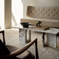 Beige tufted sofa, marble coffee table with gray and white patterns, natural woven rug, and rich brown accent chair.