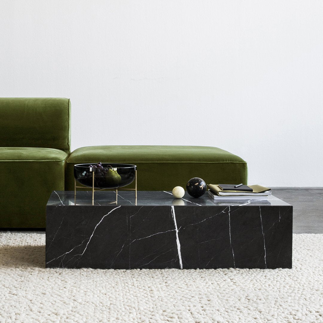 Black marble coffee table with striking white veining, complemented by a rich green velvet sofa. Neutral textured rug.