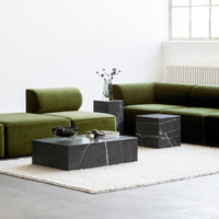 Green velvet modular sofa with black marble coffee tables, set on a textured cream area rug in a modern, minimalist space.