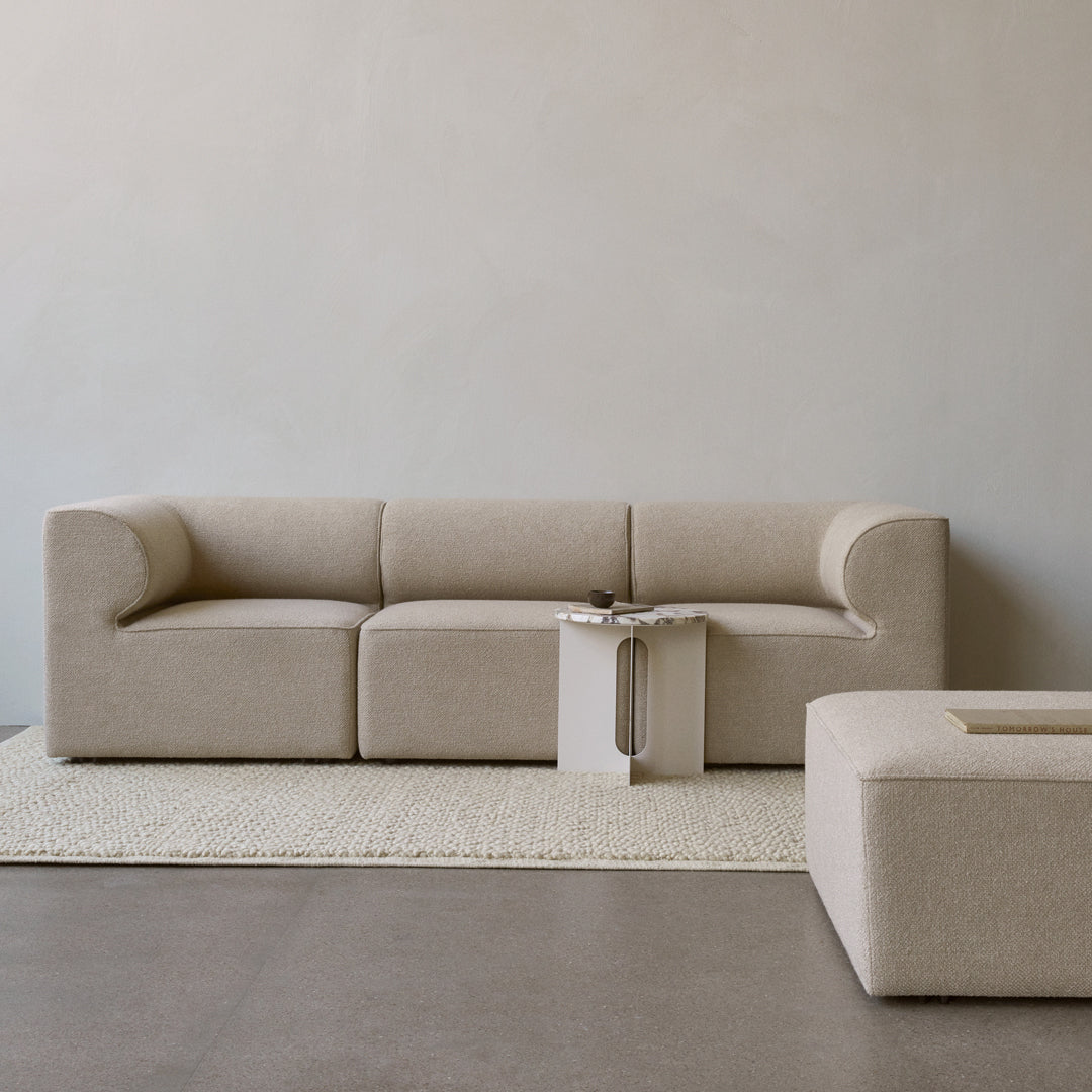 Beige sofa with rounded edges and minimalist design, paired with a textured cream rug and a geometric side table.