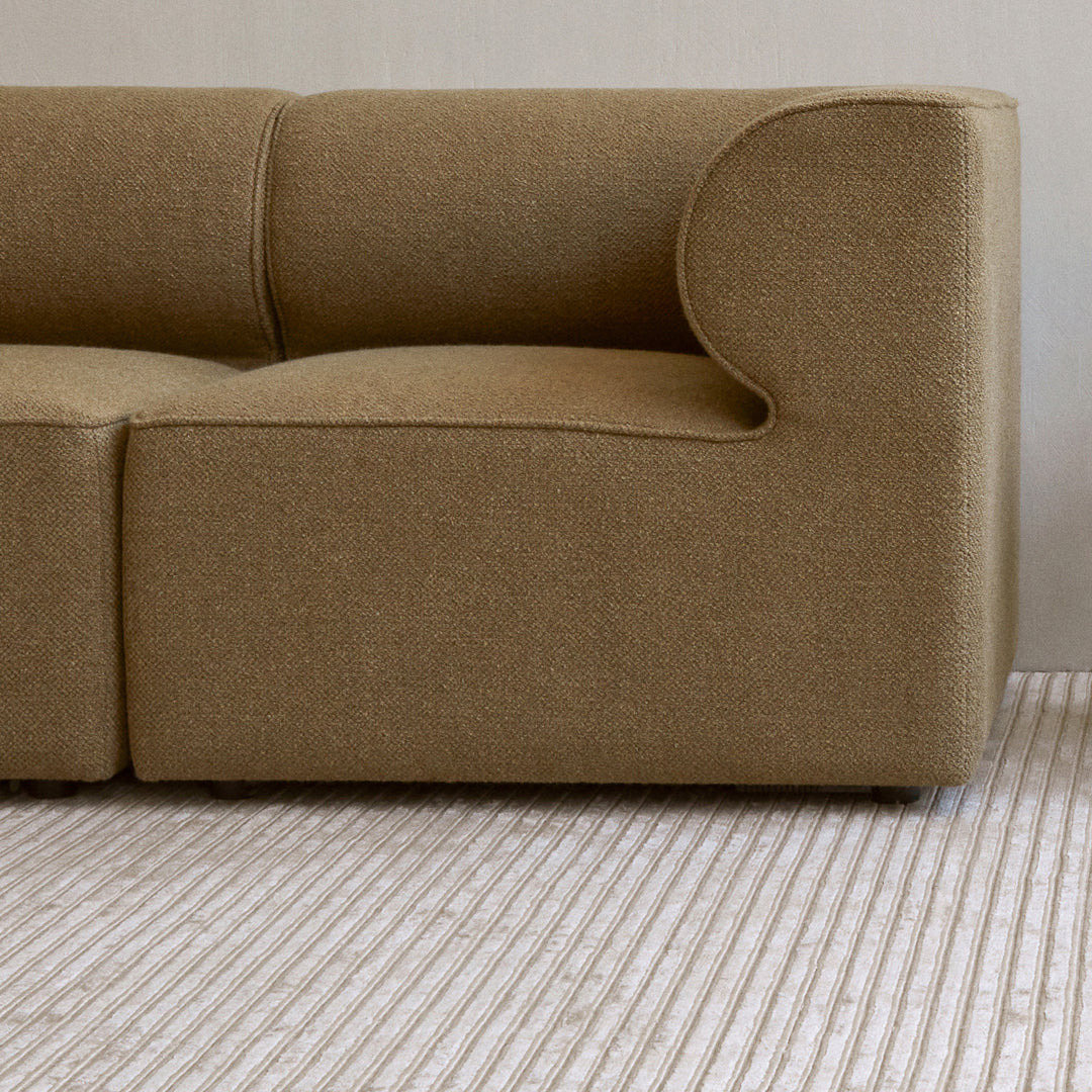 Cozy beige fabric sofa with smooth curves, paired with a textured striped rug in soft, neutral tones.