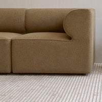 Cozy beige fabric sofa with smooth curves, paired with a textured striped rug in soft, neutral tones.
