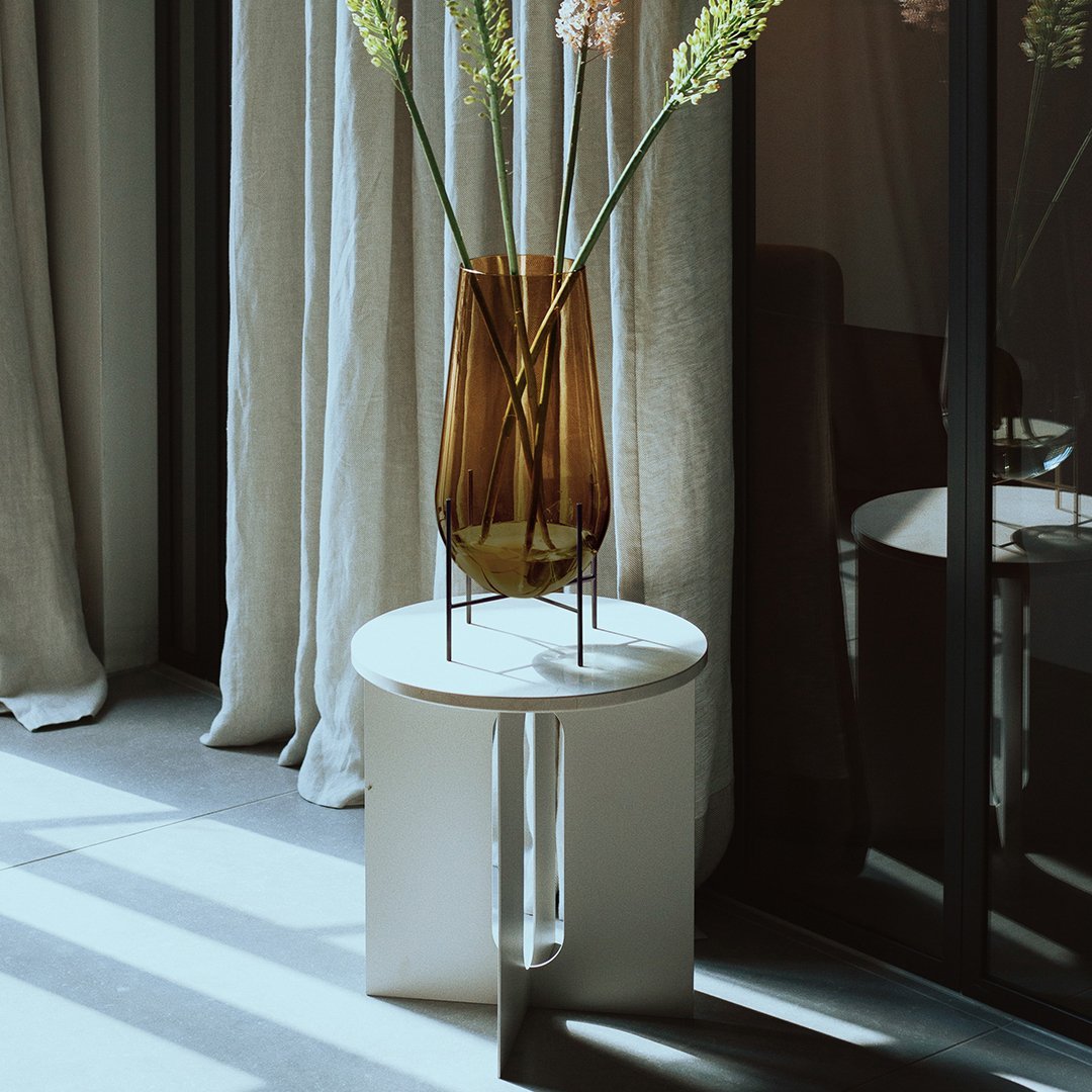 Modern white side table with a sleek design, featuring a brown glass vase and soft natural light. Stylish and contemporary.