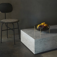 Modern gray marble coffee table with a black bowl of colorful fruits, set against a dark background. Simple, elegant design.