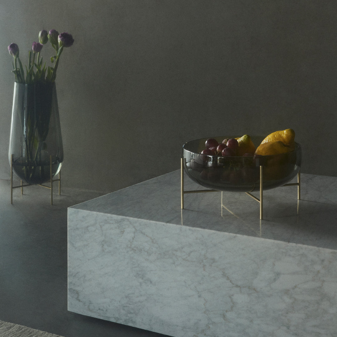 Elegant black bowl with gold accents atop a sleek marble surface, surrounded by soft purple floral arrangements.