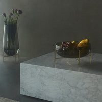 Elegant black bowl with gold accents atop a sleek marble surface, surrounded by soft purple floral arrangements.