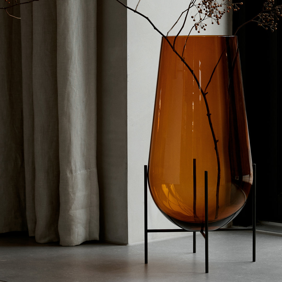 Amber-colored glass vase on a black metal stand, featuring simple lines and smooth curves. Elegant home decor accent.