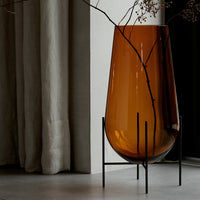 Amber-colored glass vase on a black metal stand, featuring simple lines and smooth curves. Elegant home decor accent.