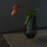 Black glass vase with a sleek design, showcasing soft pink tulips and deep green leaves against a gray backdrop.