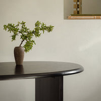 Brown textured vase with green foliage on a dark wood table against a light neutral wall. Elegant contemporary decor.