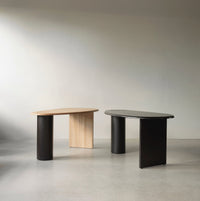 Two modern desks: one in light wood with a natural finish, the other in sleek black, featuring smooth, curved outlines.