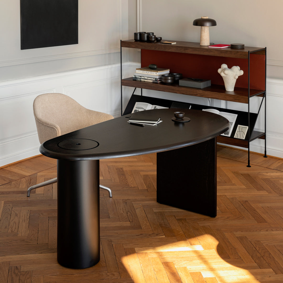 Black oval desk with wood accents, set against a light wall and warm wooden floor, creating a modern aesthetic.