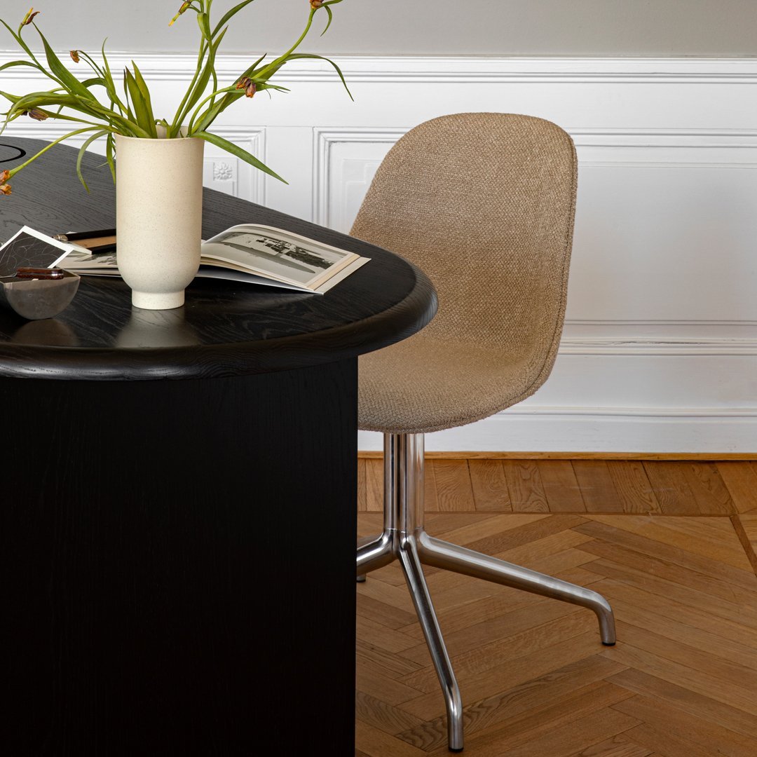 Black round table with a beige textured chair, wooden floor, and neutral-toned decorative elements.