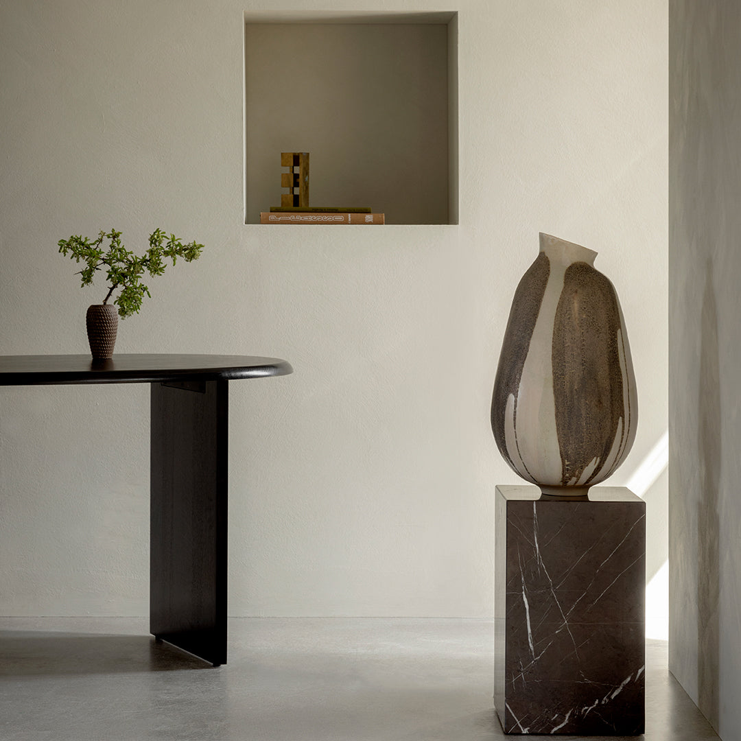 Elegant ceramic vase with beige and brown stripes, paired with a dark marble pedestal, in a minimalist interior setting.