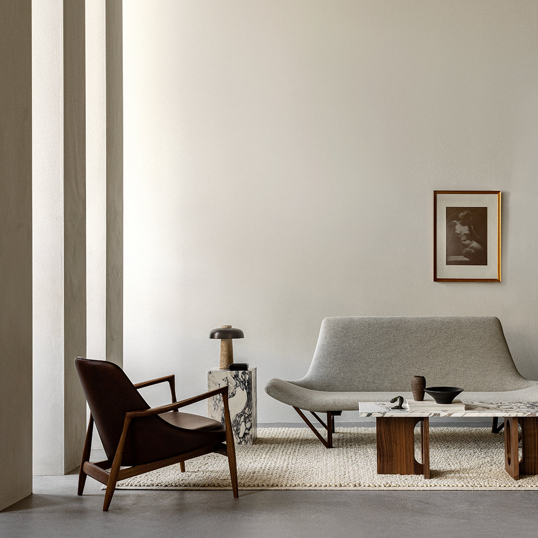 Modern living room featuring grey sofa, brown leather chair, marble accents, and neutral tones throughout.
