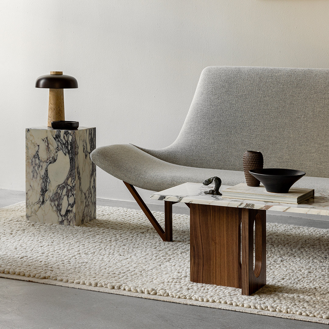 Gray curved sofa, white shag rug, marble table with black and brown accents, natural wood elements for modern decor.