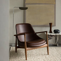 Brown leather chair with smooth curves and wooden legs, paired with a neutral-toned woven rug and minimal decor.