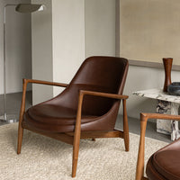 Brown leather chair with mid-century wooden frame, set on a textured beige rug in a modern interior.